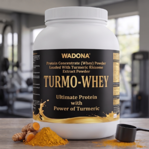 A container of Wadona Turmo-Whey Premium Turmeric Whey Protein on a wooden table with turmeric roots and powder in a gym setting.